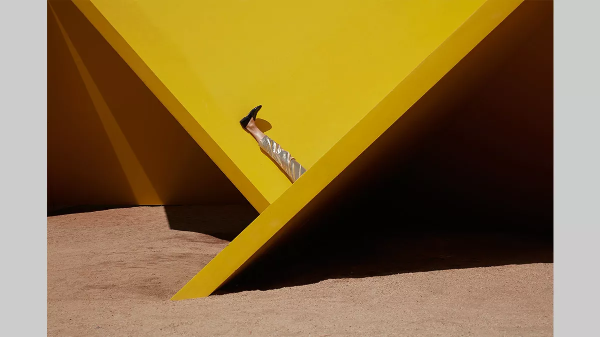 A pair of legs laying upwards on a geometric sculpture. The rest of the figure is hidden from view.