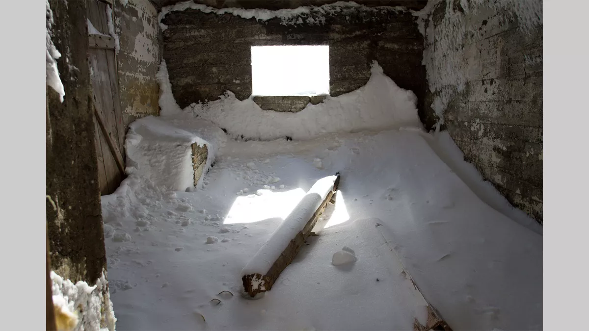 Inside a derelict building, filled with piles of timber covered in snow.