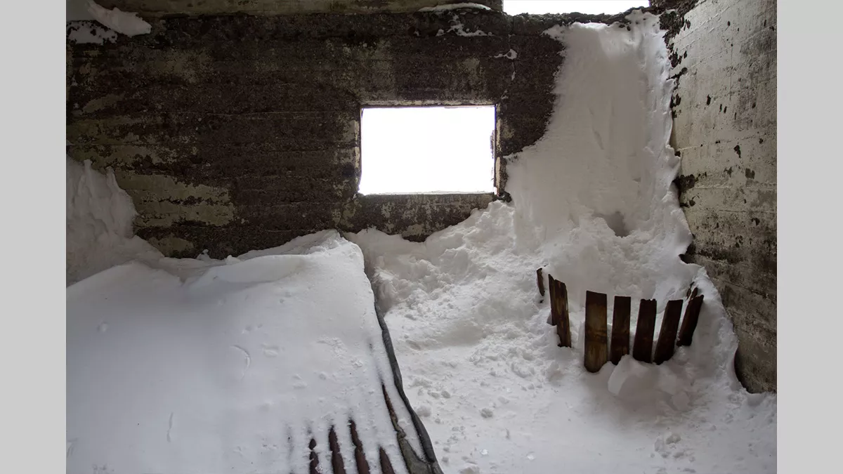 Inside a derelict building, filled with piles of timber covered in snow.