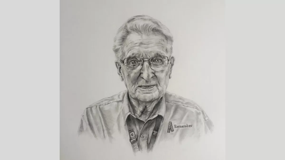 Older man looking straight forward, wearing glasses. He is wearing a lanyard, and his shirt has "remember" and an awareness ribbon embroidered on it.