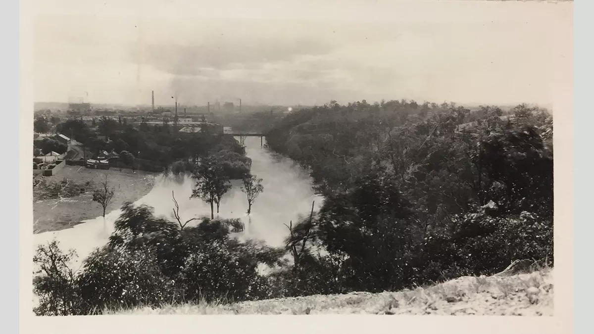 Photo looking down on a river and landscape from a hill industrial buildings on the skyline