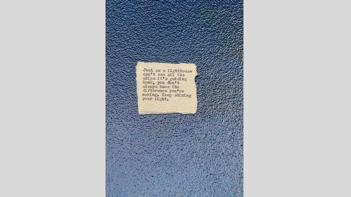 A piece of torn paper with a poem printed from a typewriter, sitting on a blue shiny textured surface