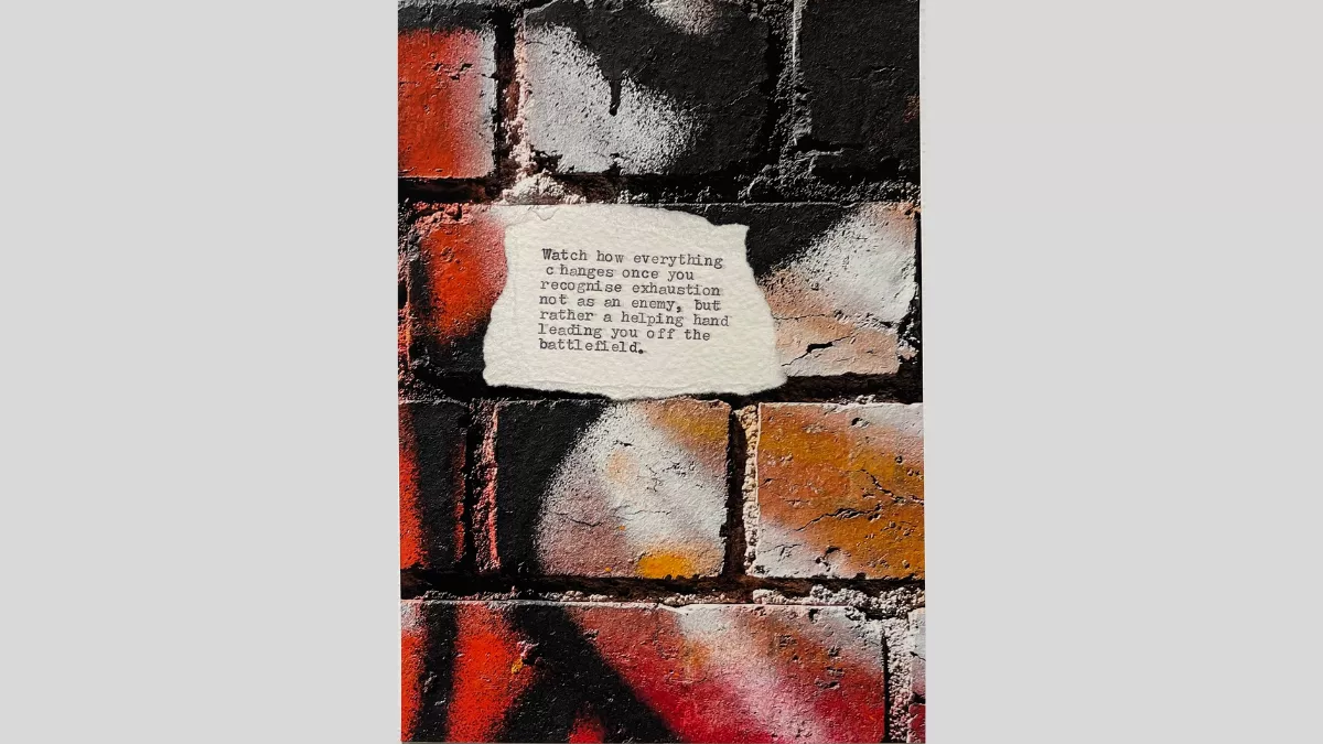 A piece of torn paper with a poem printed from a typewriter, sitting on a brick surface that has been grafittied with black, red, white and orange spray paint