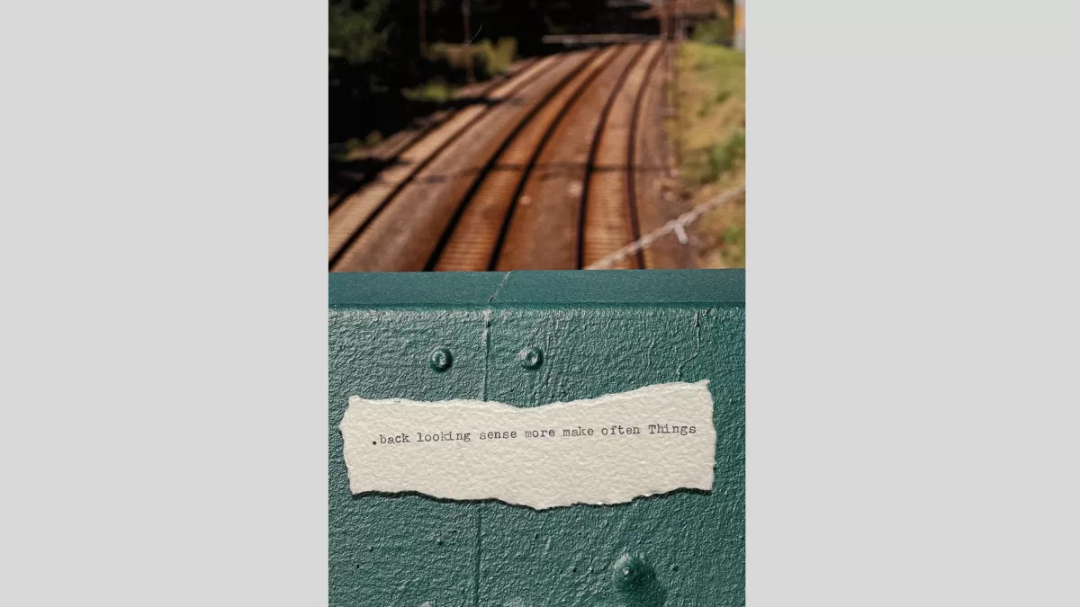 A piece of torn paper with a short piece of text printed from a typewriter, sitting on the site of a fence overlooking a traintrck that goes underneath the fence