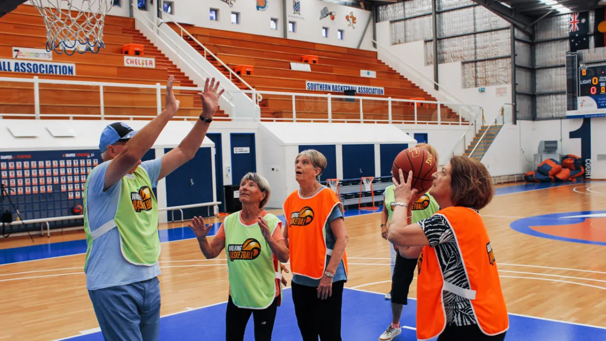 A group of older adults on a basketball court wearing bibs and playing walking basketball