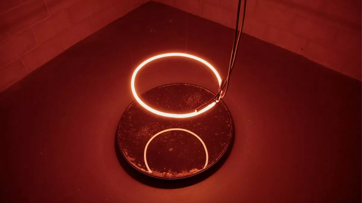 A red led-light circle hanging over a mirror in a dark corner reflecting the red light in all directions