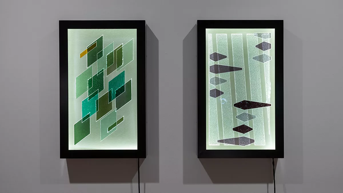 Two vertical-rectangular artworks on a wall. One features scattered grey and black diamond shapes and one features green overlapping diamond shapes.