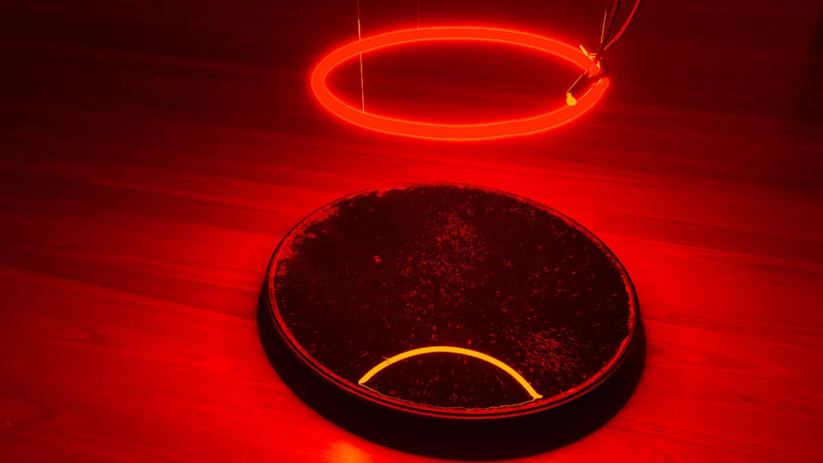 Art installation featuring a red illuminated circle hanging over a black reflective circle on the ground.