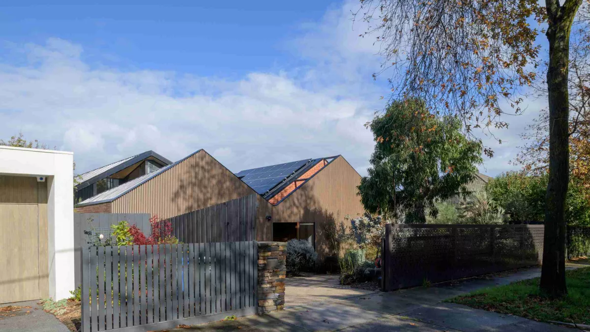 2 houses clad in wood and shaped like barns with solar panels on roof