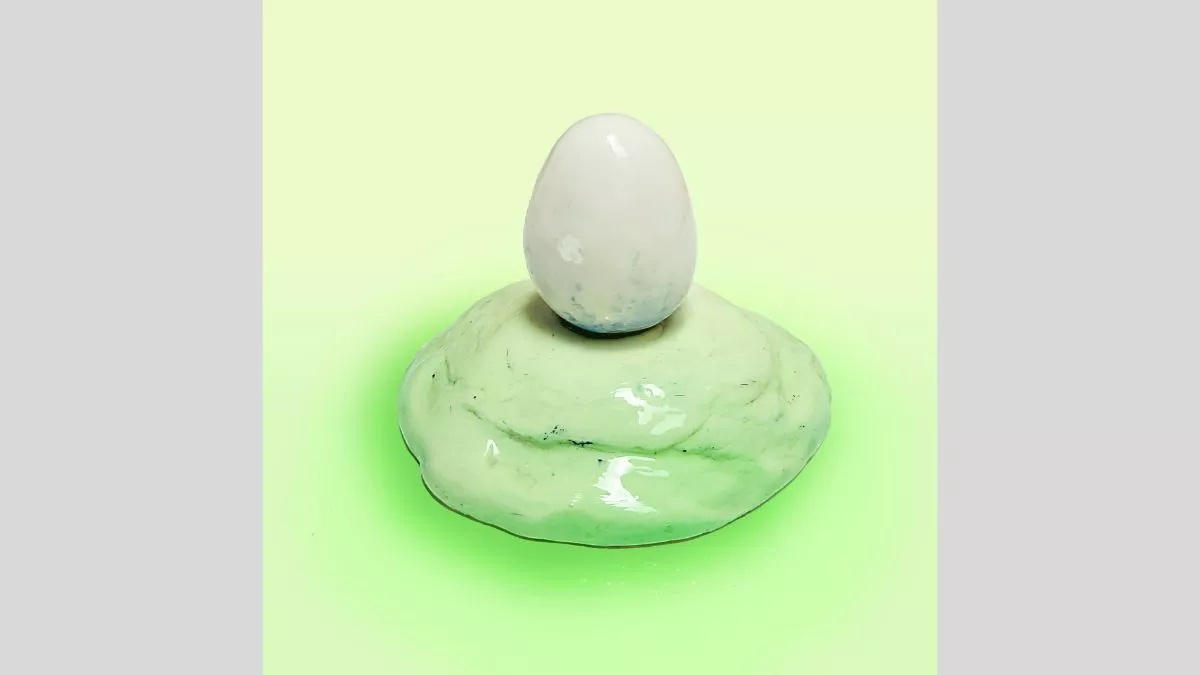 Ceramic sculpture of a white egg on a light green mound.&nbsp;