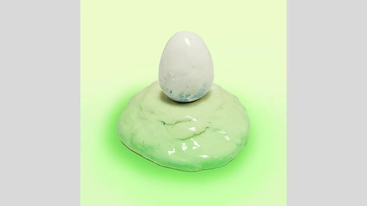 Ceramic sculpture of a white egg on a light green mound.&nbsp;