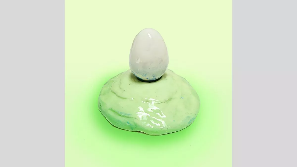 Ceramic sculpture of a white egg on a light green mound.&nbsp;