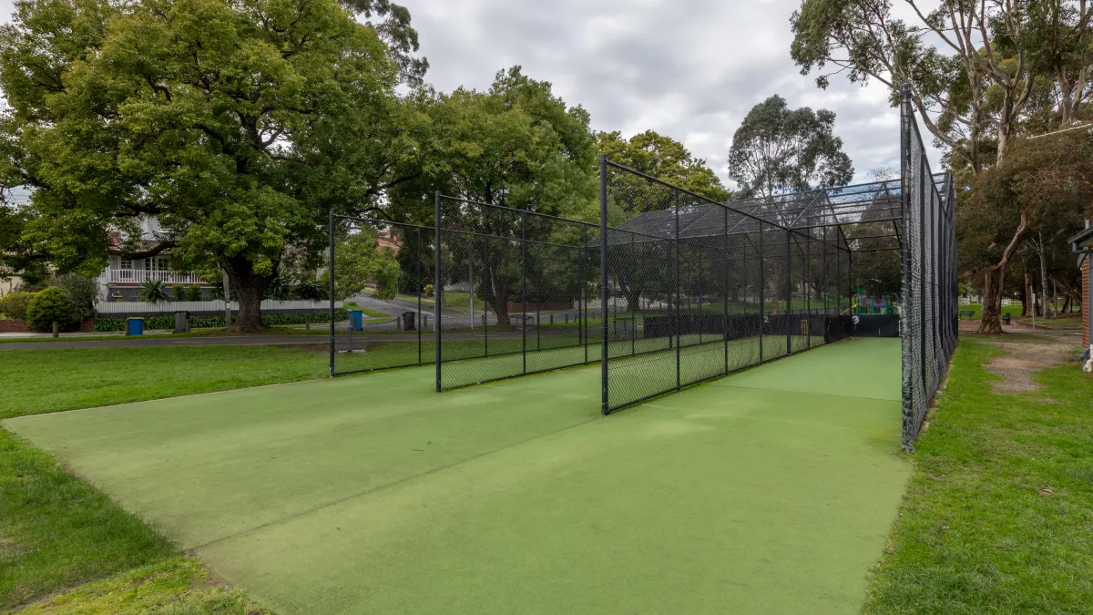 Cricket nets with three lanes divided by tall black fencing. There are tall trees in the background.