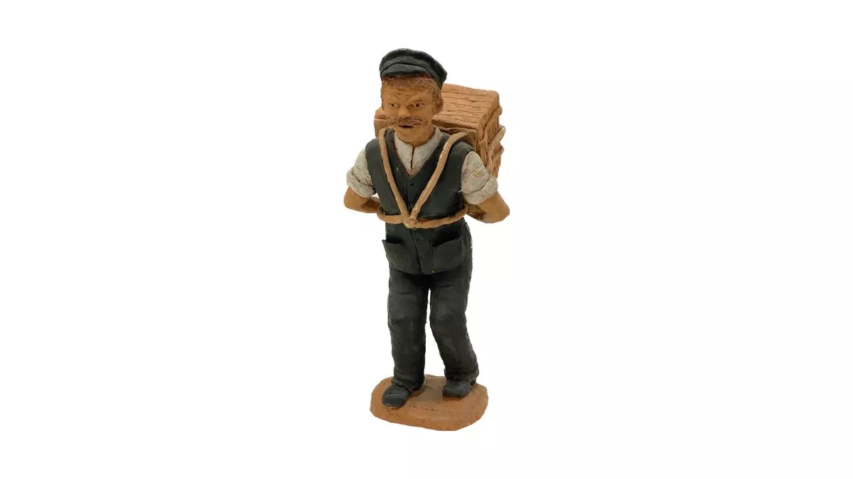Clay sculpture of a man wearing a work uniform including a white shirt, dark grey vest, pants, boots and cap. A large case is suspended on his back with cords attached to the case strapped across his chest and his arms bent back to support the weight.