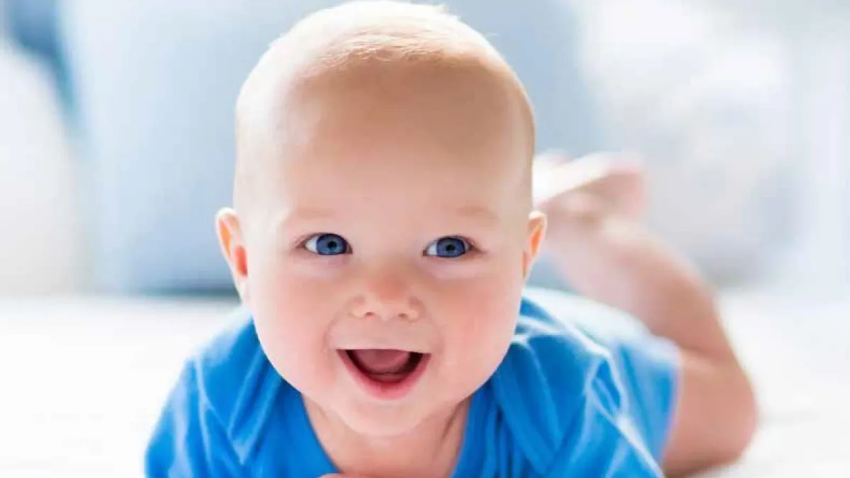 Smiling baby with blue eyes and blue clothing, lying on the stomach.