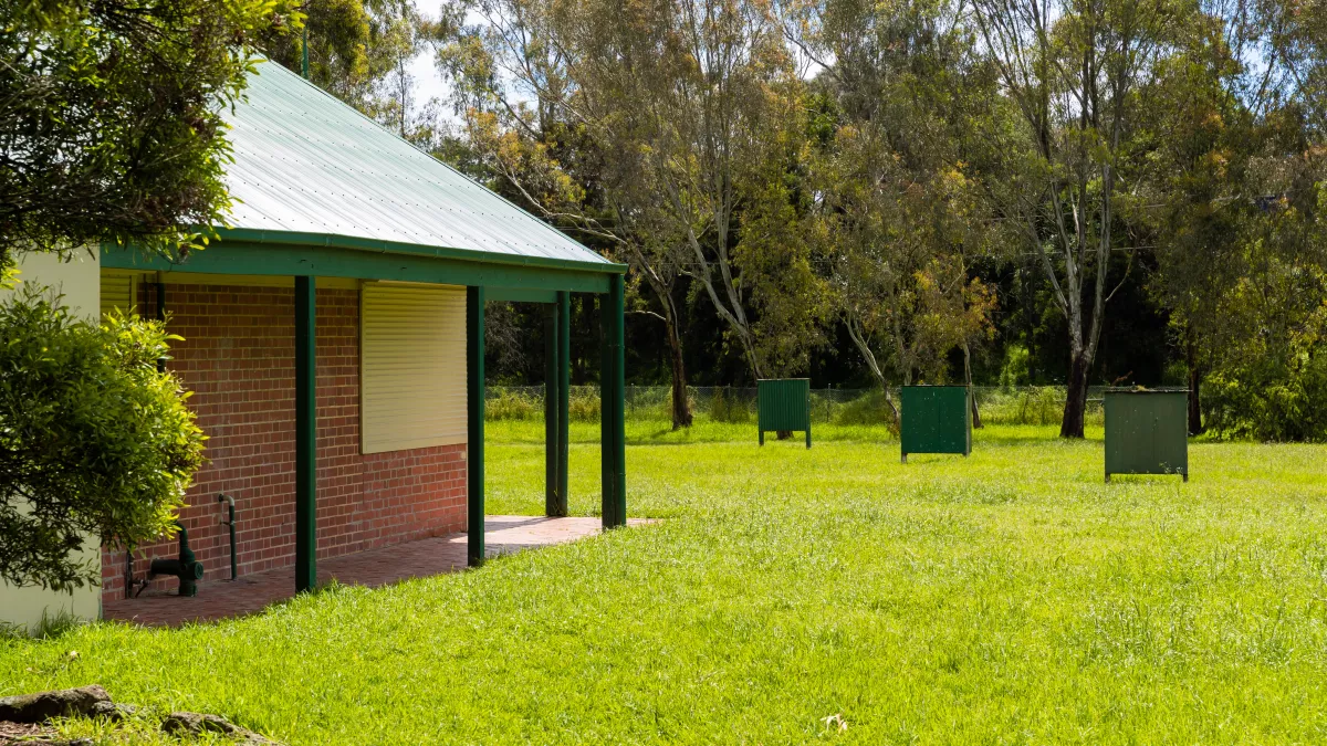 Grass area with part of a small building visible to the left. There are 3 archery targets in the distance.