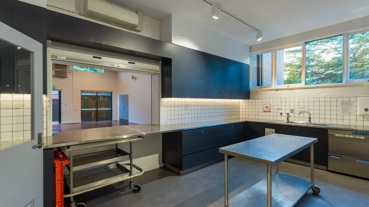 A kitchen space with benches, dishwasher, sink and kitchen island. Part of the kitchen is open to an adjoining room.