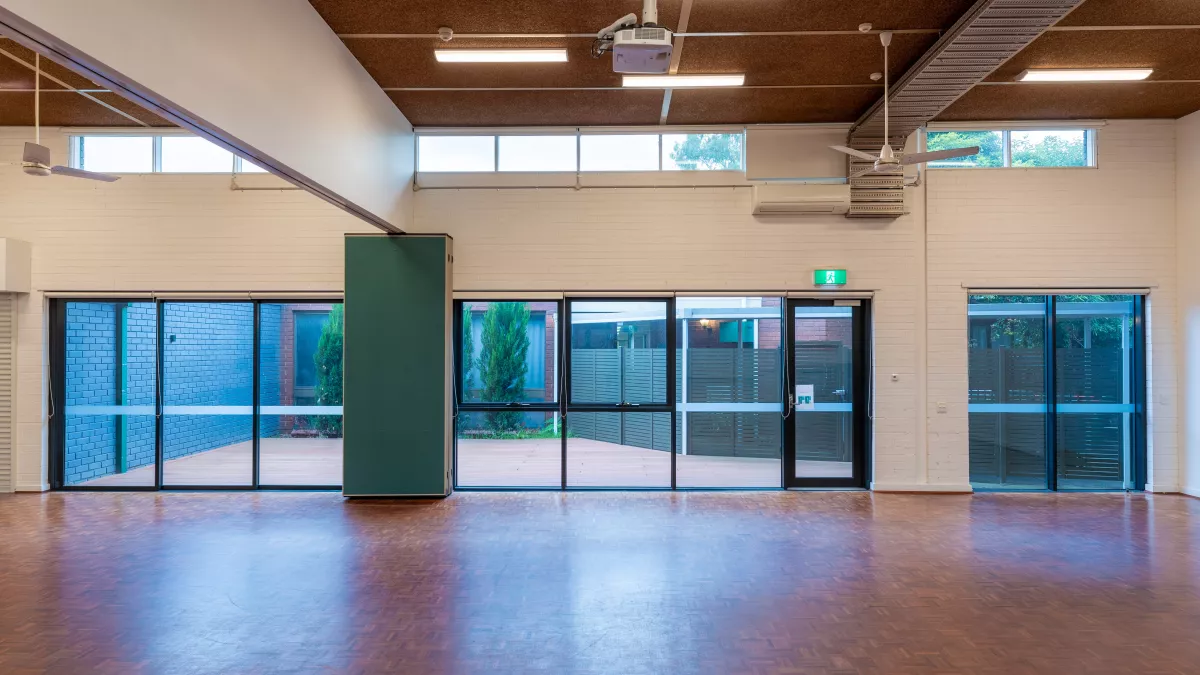 A large room with wooden floors. A patio area can be seen through the large windows. 