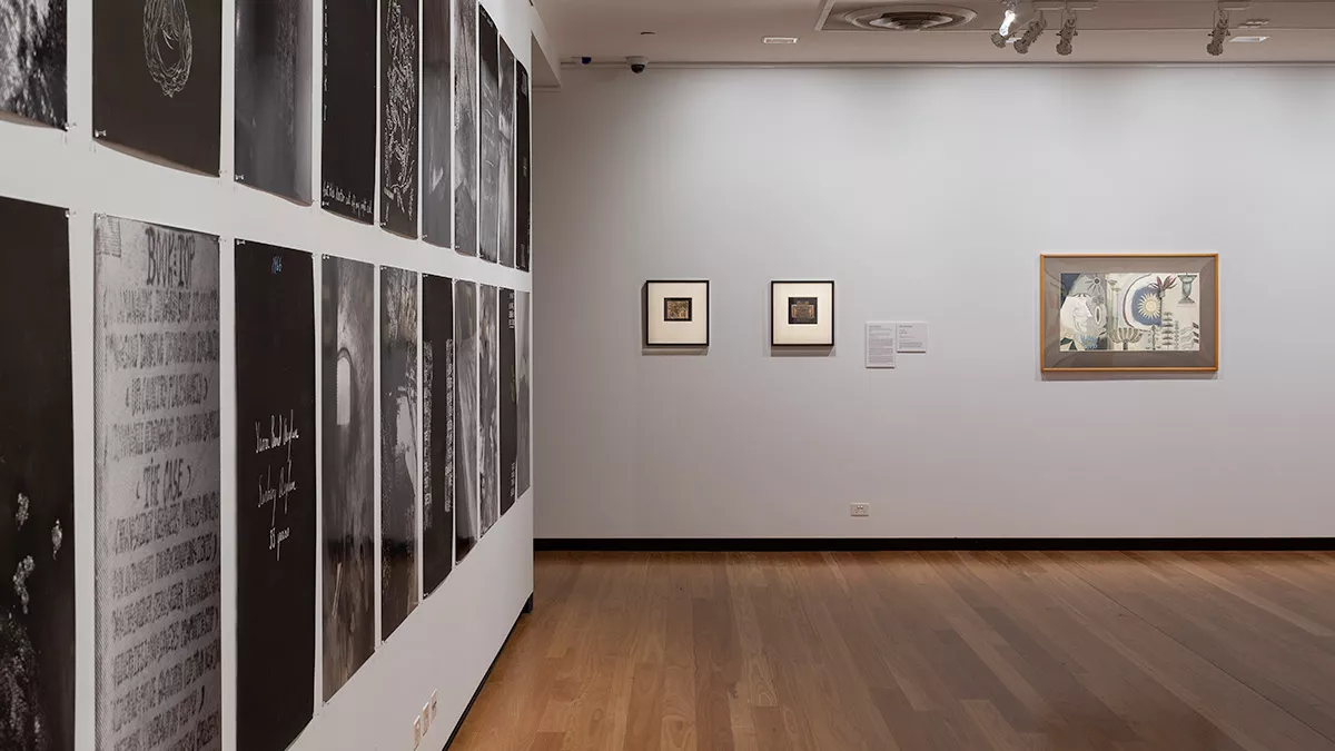 a wall of black and while images hung close together. on the far wall are two small paintings.