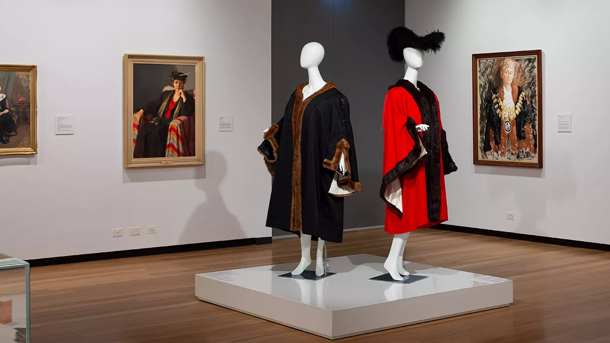 mayoral robes including a hat. Paintings on the walls behind of previous municipal mayors wearing the robes