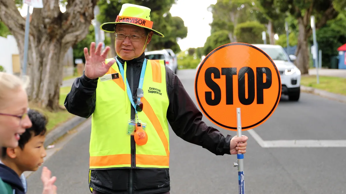 Man in fluorescent uniform with a stop sign helping children cross the road