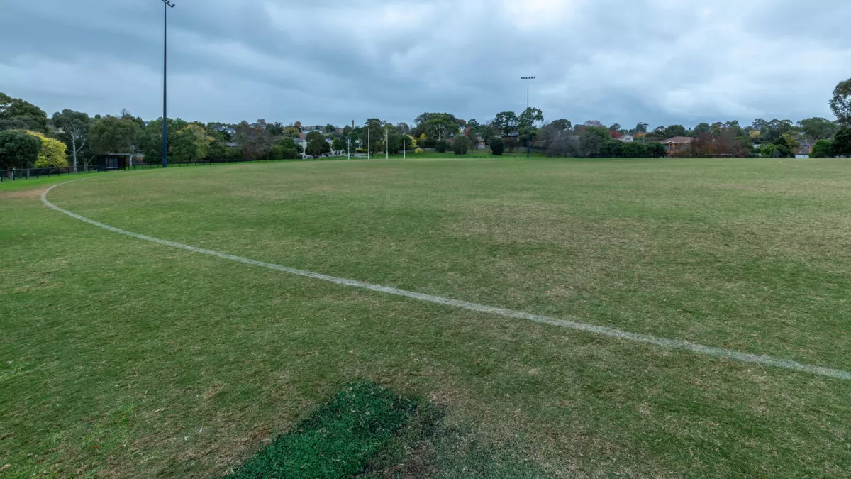 A sports ovval with white line markings. Trees can be seen in the background. 