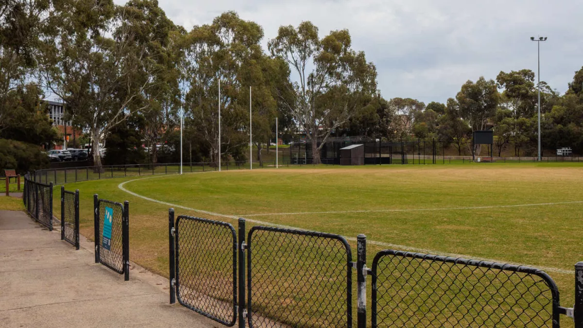 A fenced sports field with line markings, AFL goal posts and sportsground lighting.
