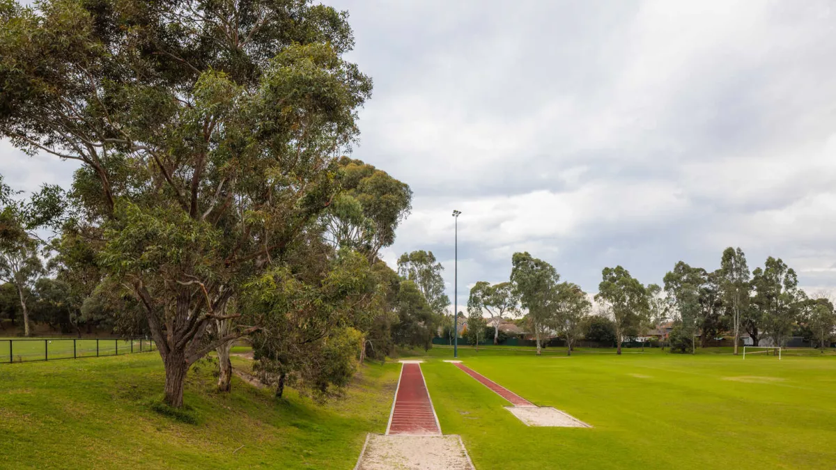 2 red atheletics tracks both with sand pits at the end. Tall trees are to the left, and a sportsground is to the right of the tracks