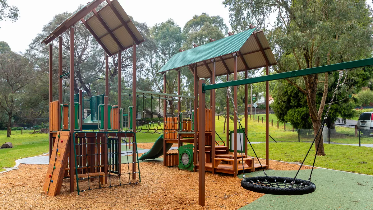 a basket swing and 2 covered slides and climbing frames at a playground