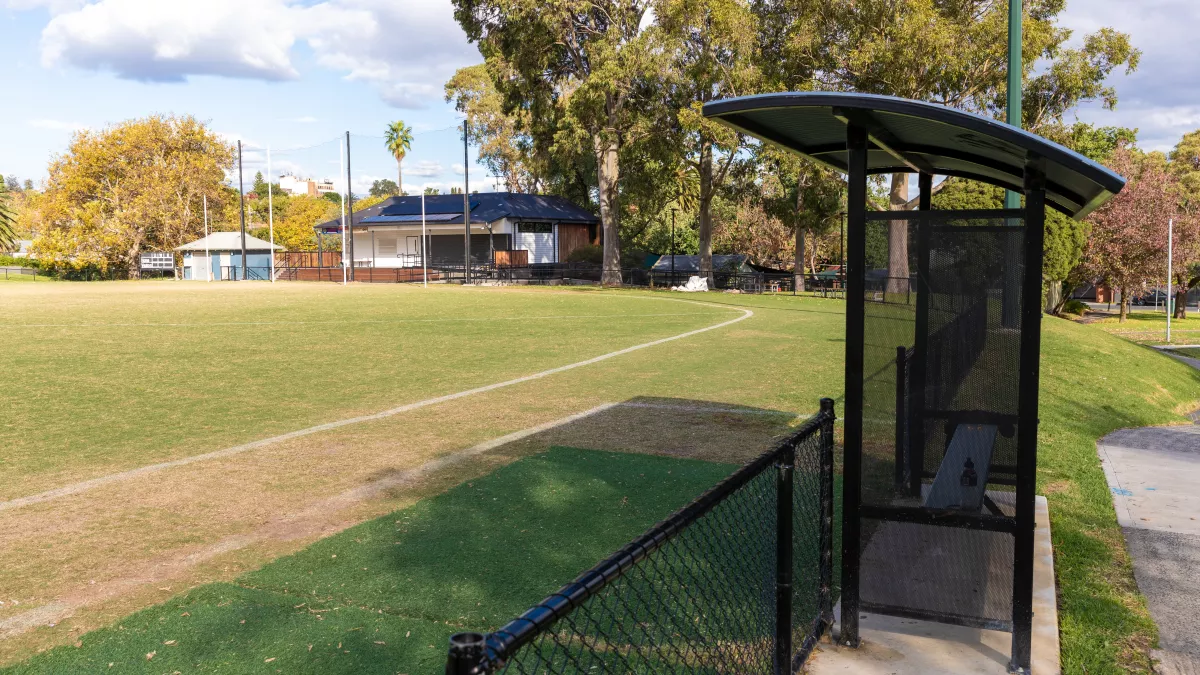 A sheltered bench on the perimeter of a sportsground