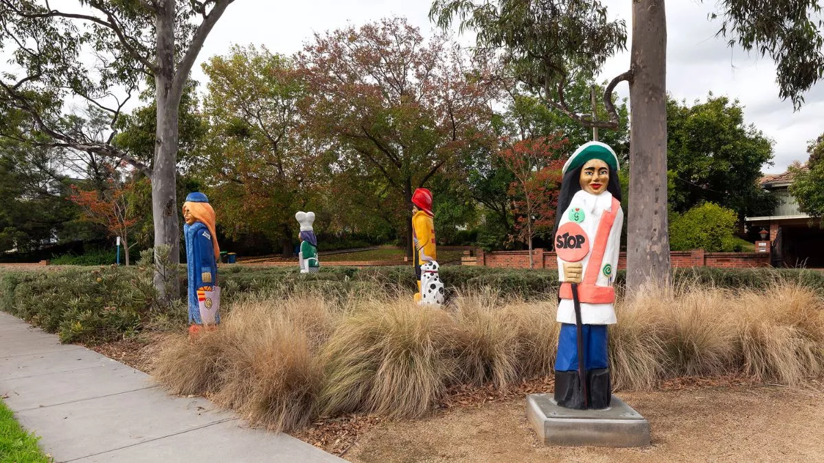 four colourful figures and a dalmatian carved from wood. The figures are in a grassy park. The figure in the foreground holds a stop sign