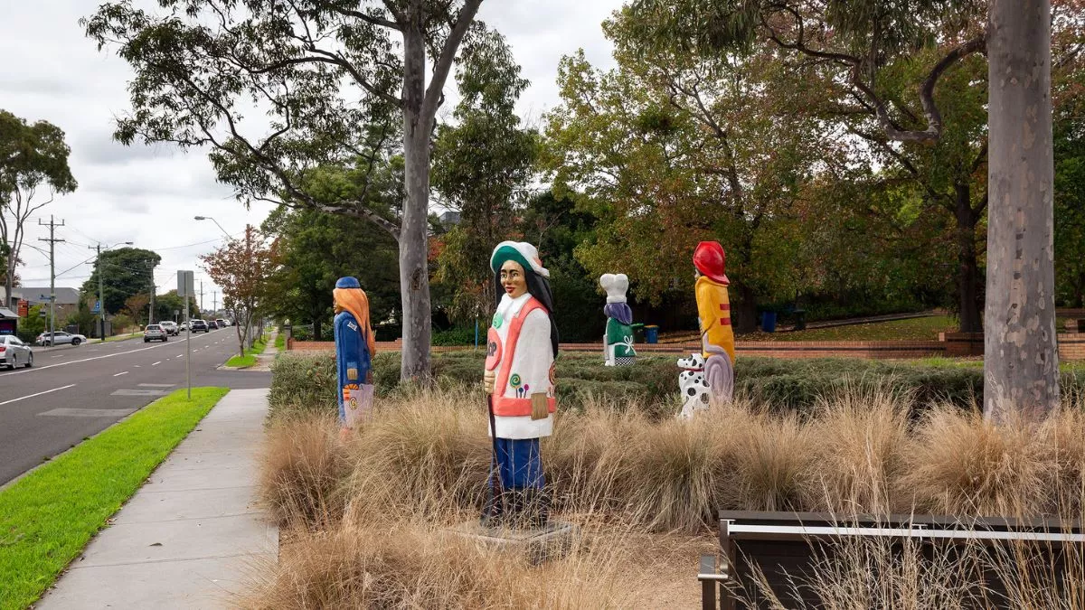 four colourful figures and a dalmatian carved from wood. The figures are in a grassy park. The figure in the foreground holds a stop sign