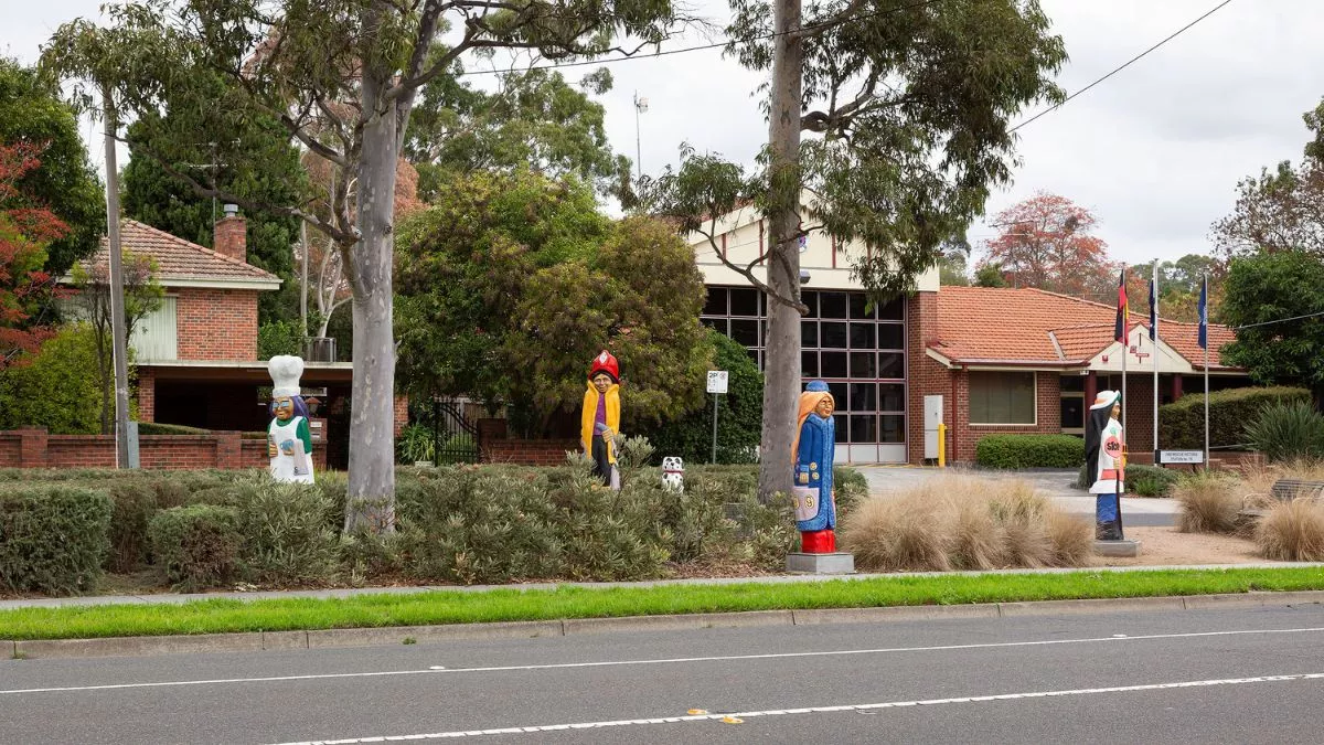 four colourful figures and a dalmatian carved from wood. The figures are in a grassy park.