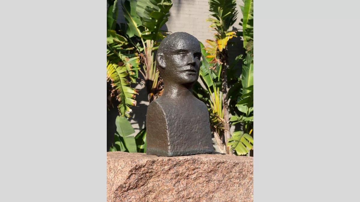 a small bronze bust of a figure sitting on top of an orange stone.