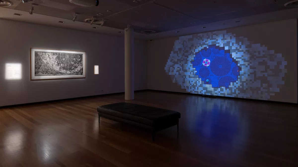 A dark gallery space with an intricate black and white print and a glowing digital projection of a blue, pixelated geometric portal.