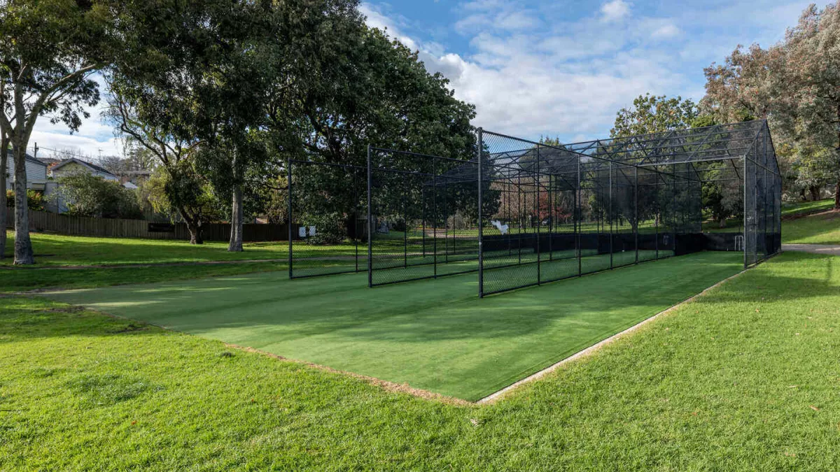 3 cricket net lanes on synthetic turf surrounded by tall trees and grass.