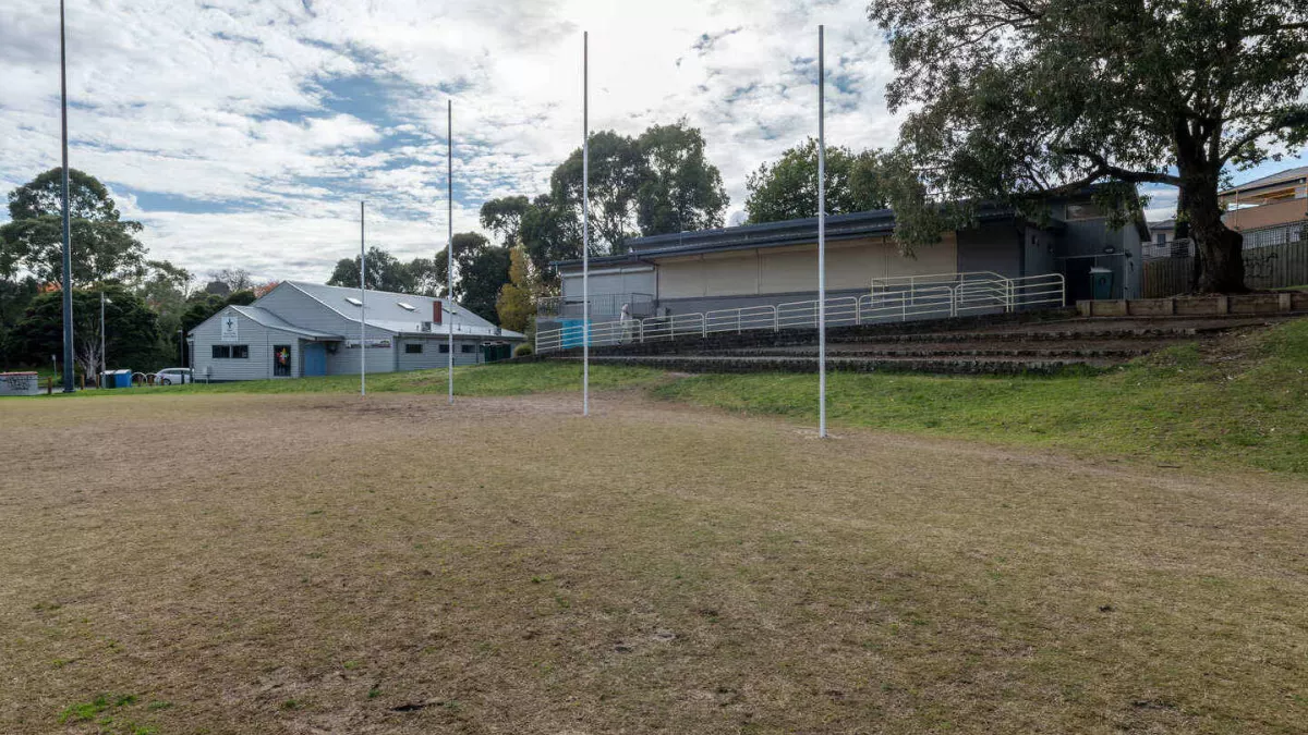 A sportsground looking towards 4 AFL goal posts. 2 buildings are in the background.