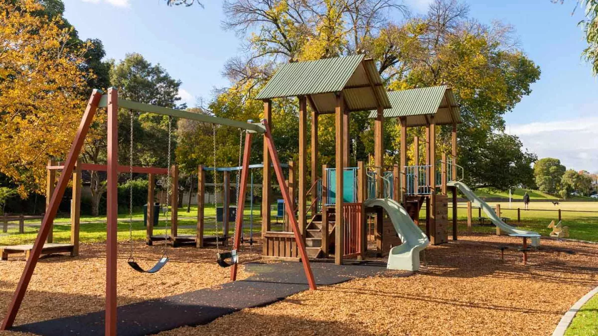 A playground in a park featuring swings and 2 slides