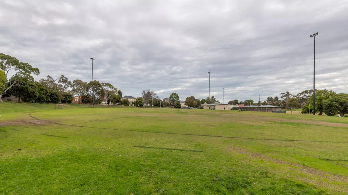 A circular sportsground. A building and another field is in the background.