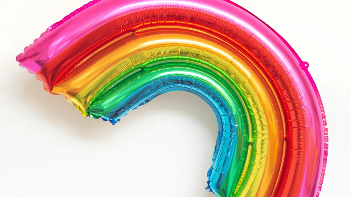 a foil balloon in the shape and colours of a rainbow being held up high by a hand