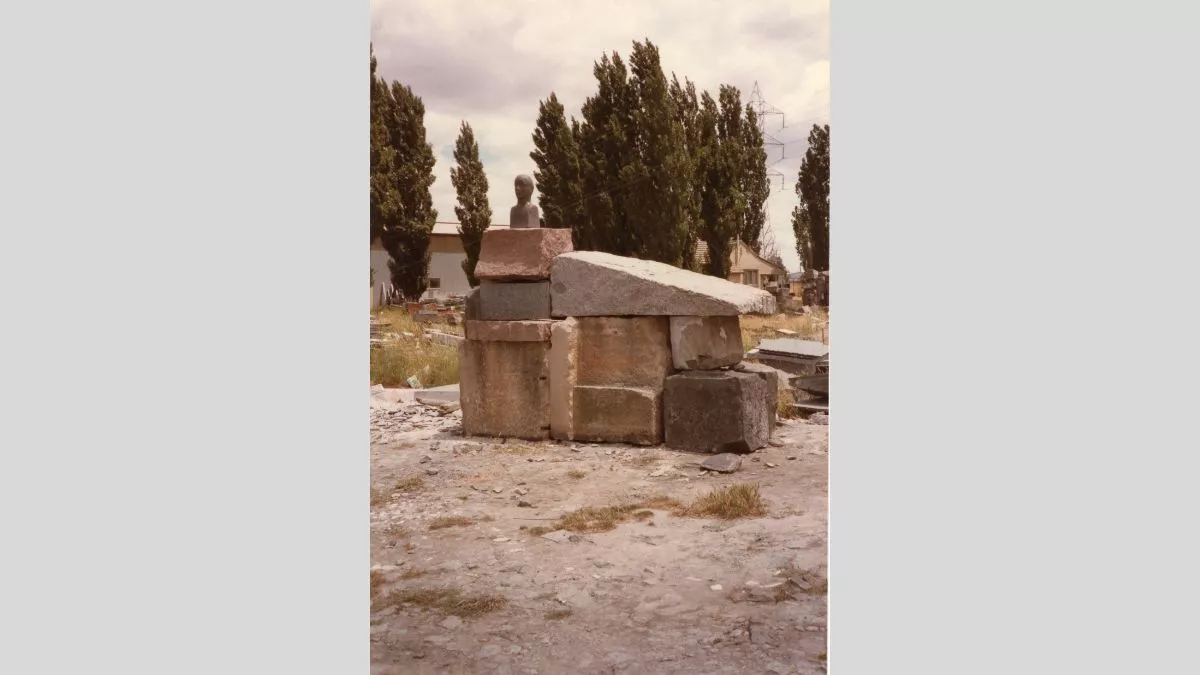 A pile of stones with a bronze bust on top, sit in a field.