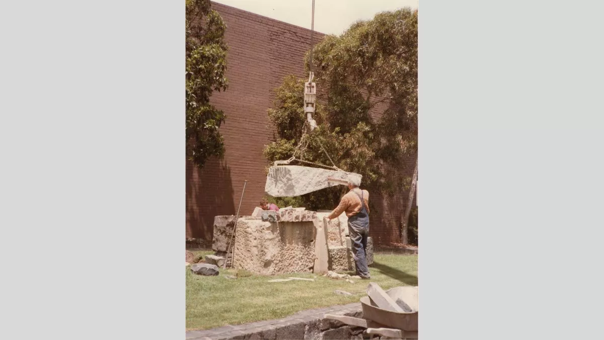 Two figures position large stones with the assistance of a crane.