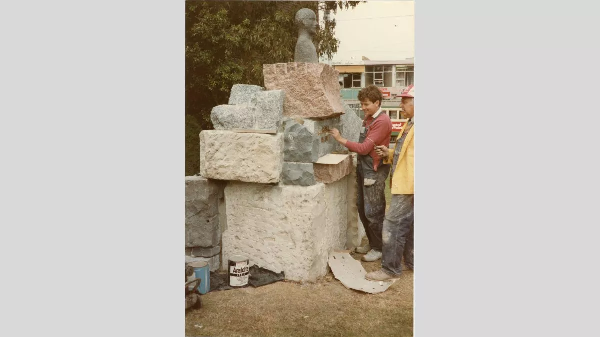 Two figures add letter to a sculpture made form large chunks of stone