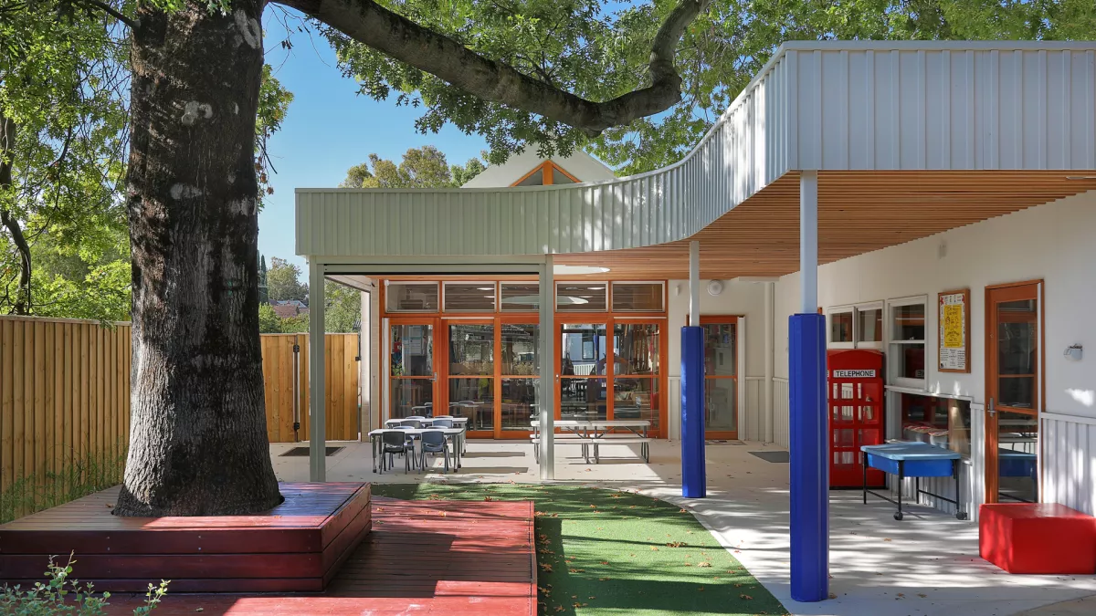 Outdoor area of a modern building with a large tree, seating, and a red phone booth.