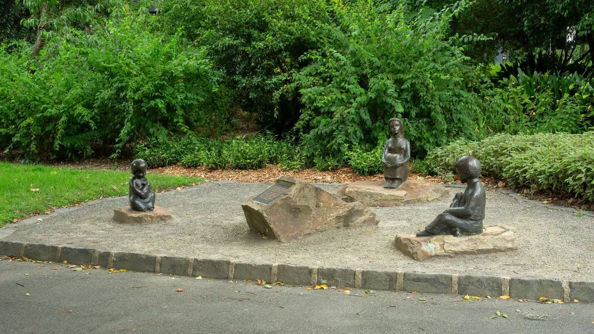 Three bronze figures of children positioned around a central plaque. Green leaves make up the backdrop