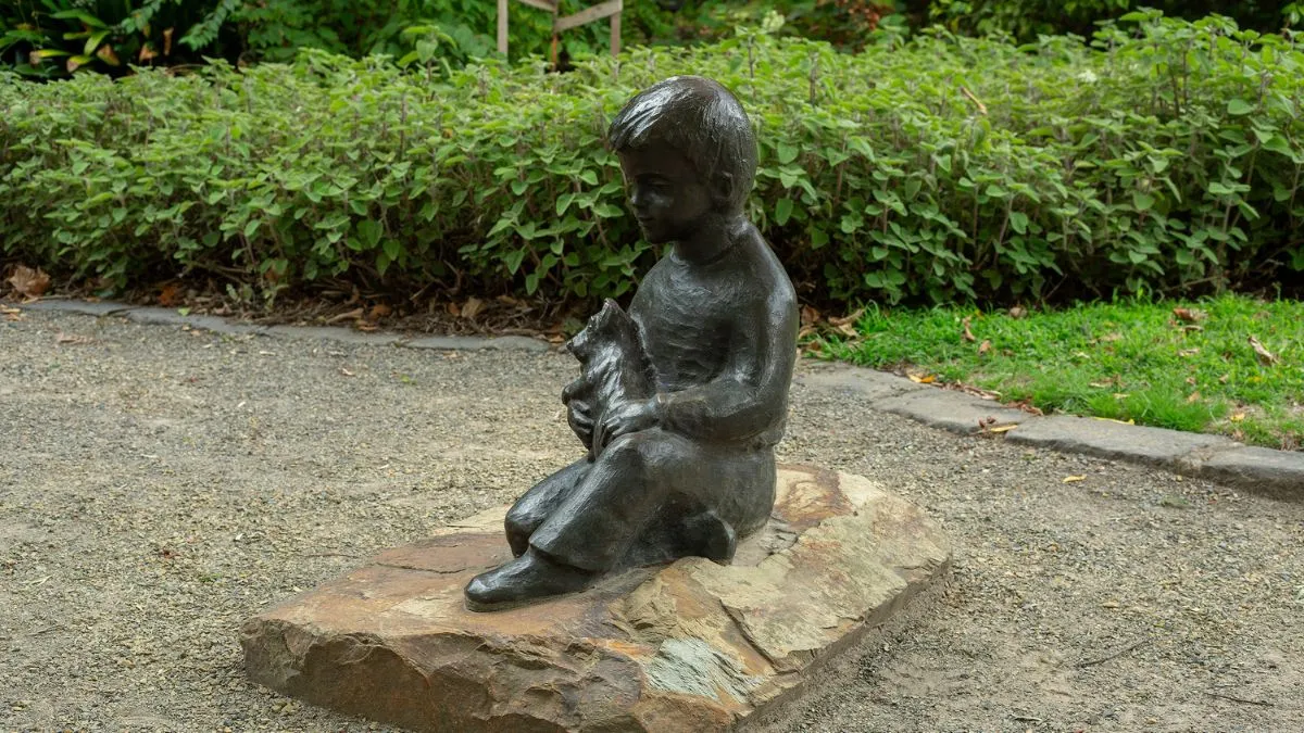 A bronze statue of a boy holding a dog in his lap. The statue is attached to a large piece of stone.