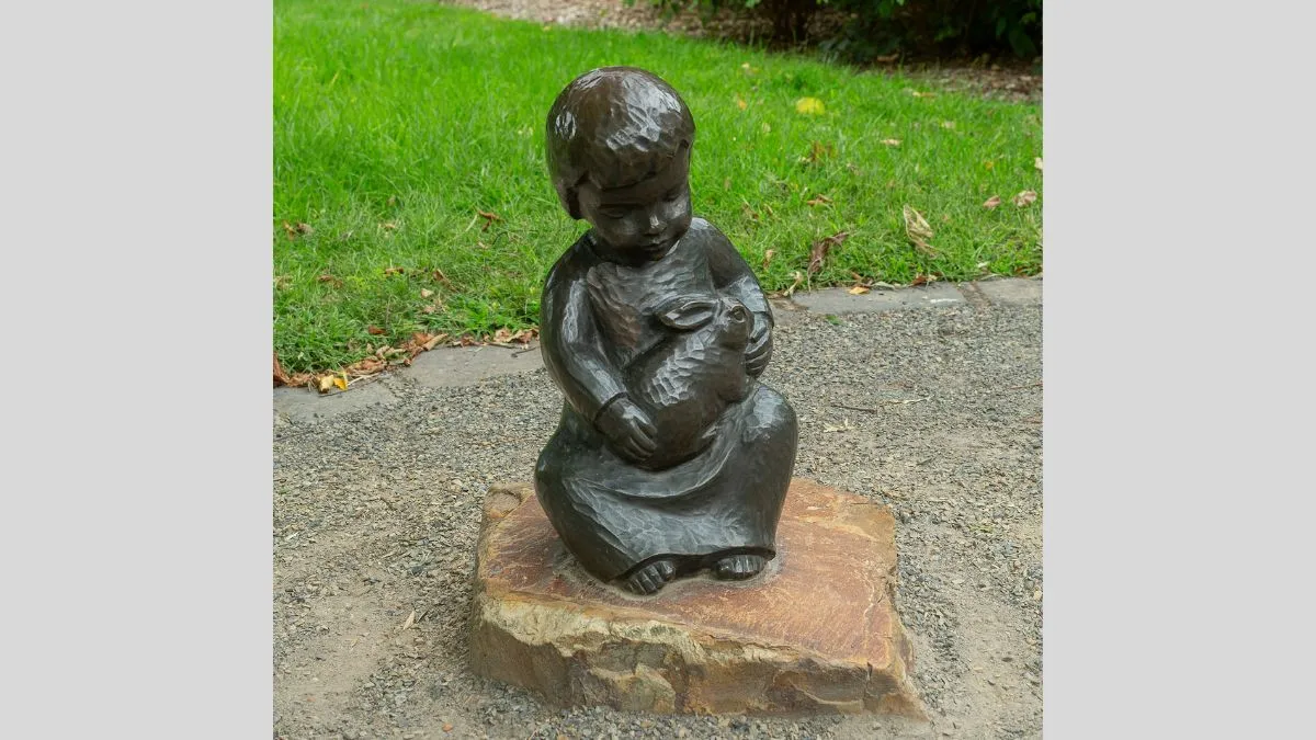 A bronze statue of a small child holding a rabbit in its lap. The statue is attached to a large piece of stone.