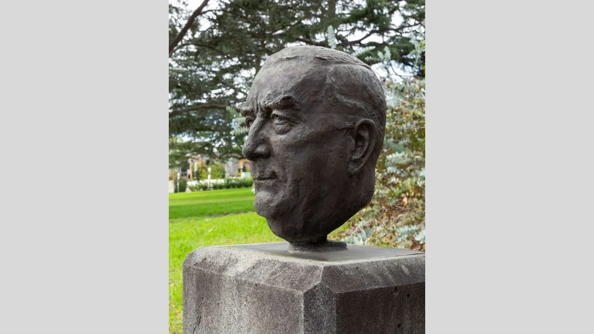 A small bronze head of a man with short hair. The head is attached to a rectangular column