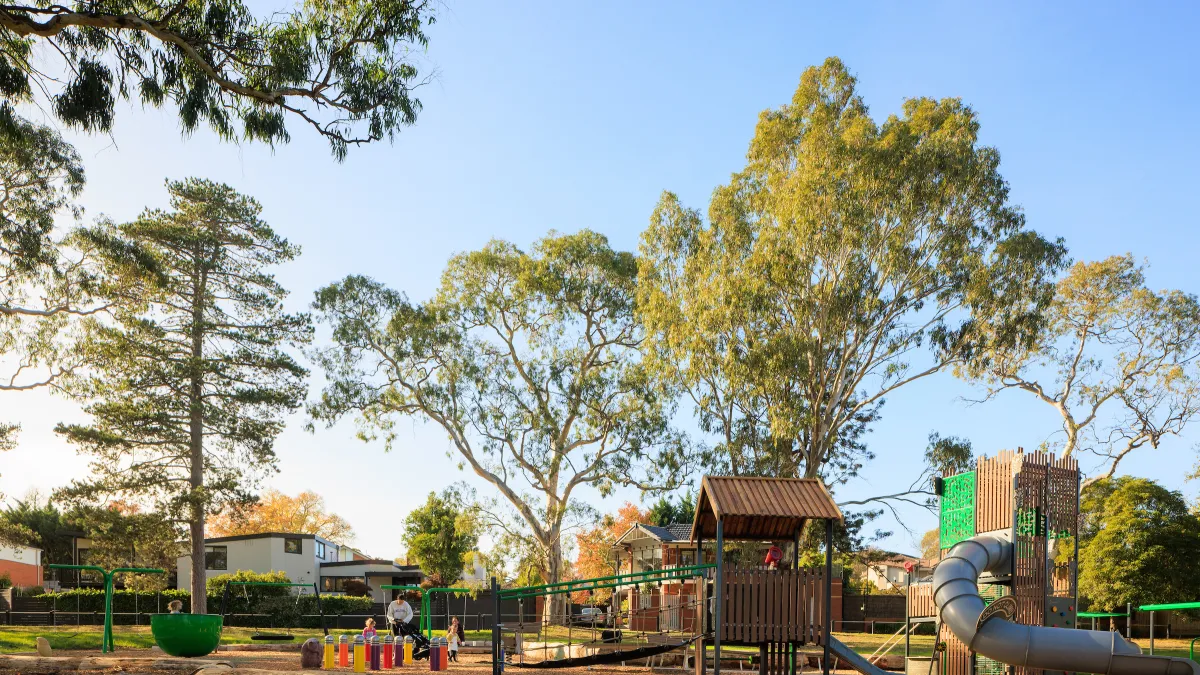 a small playground fringed with large trees in the fading light