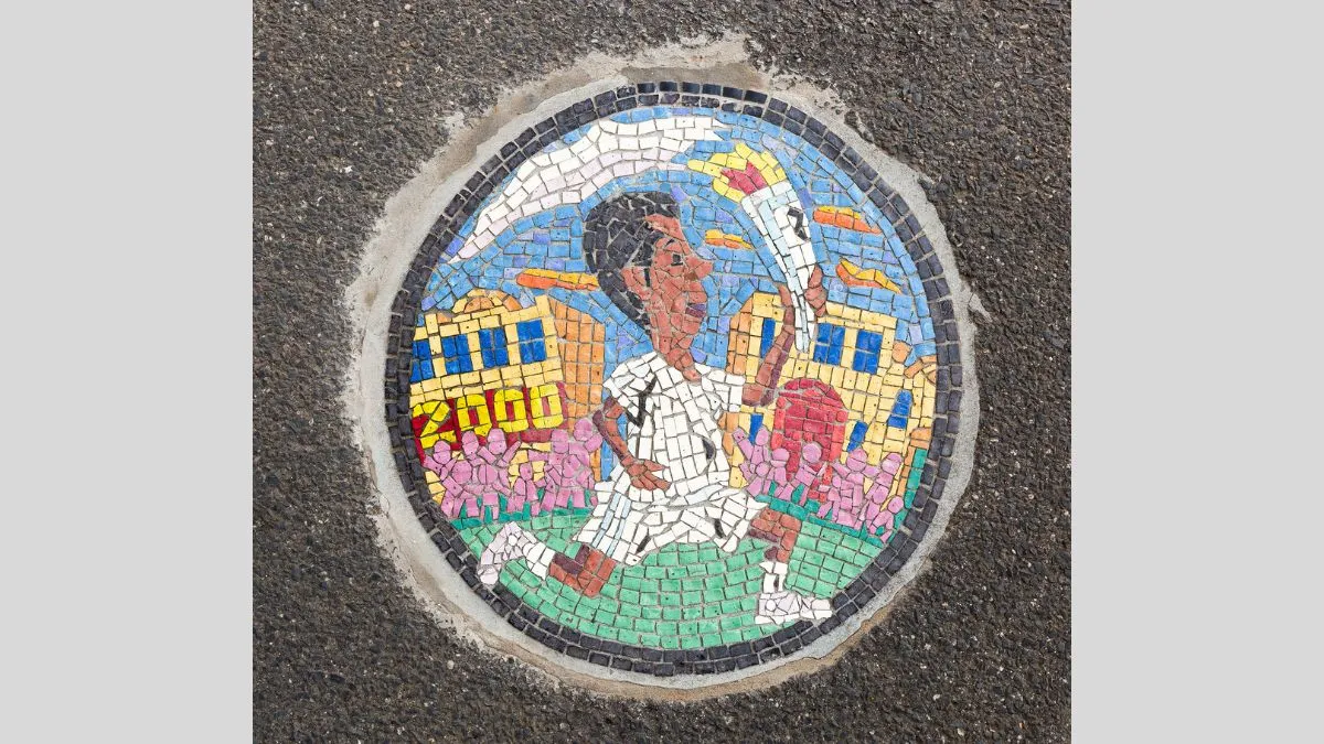 Tile mosaic embedded in footpath of a man in white carrying a flaming torch